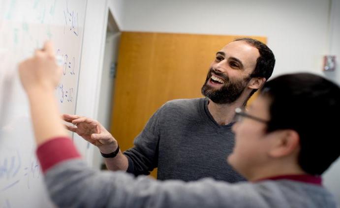 一位亿德体育的教授在教室里帮助学生在白板上解数学方程.